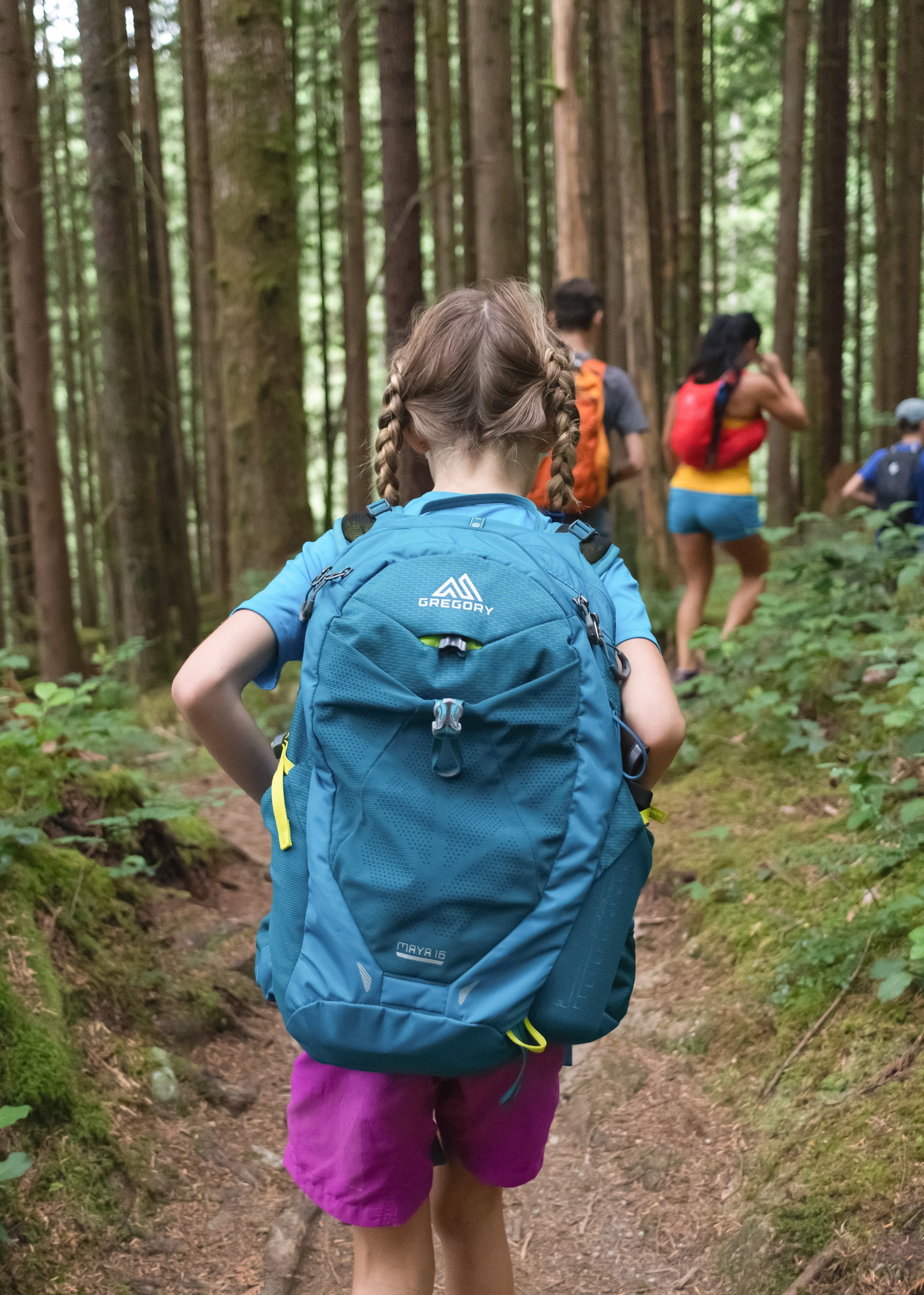 Cute little girl with a backpack happily walking into the woods among a group of hikers.